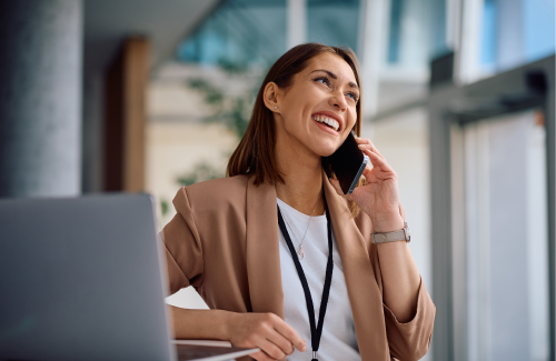 A woman in an office talking on a cellphone and smiling. 